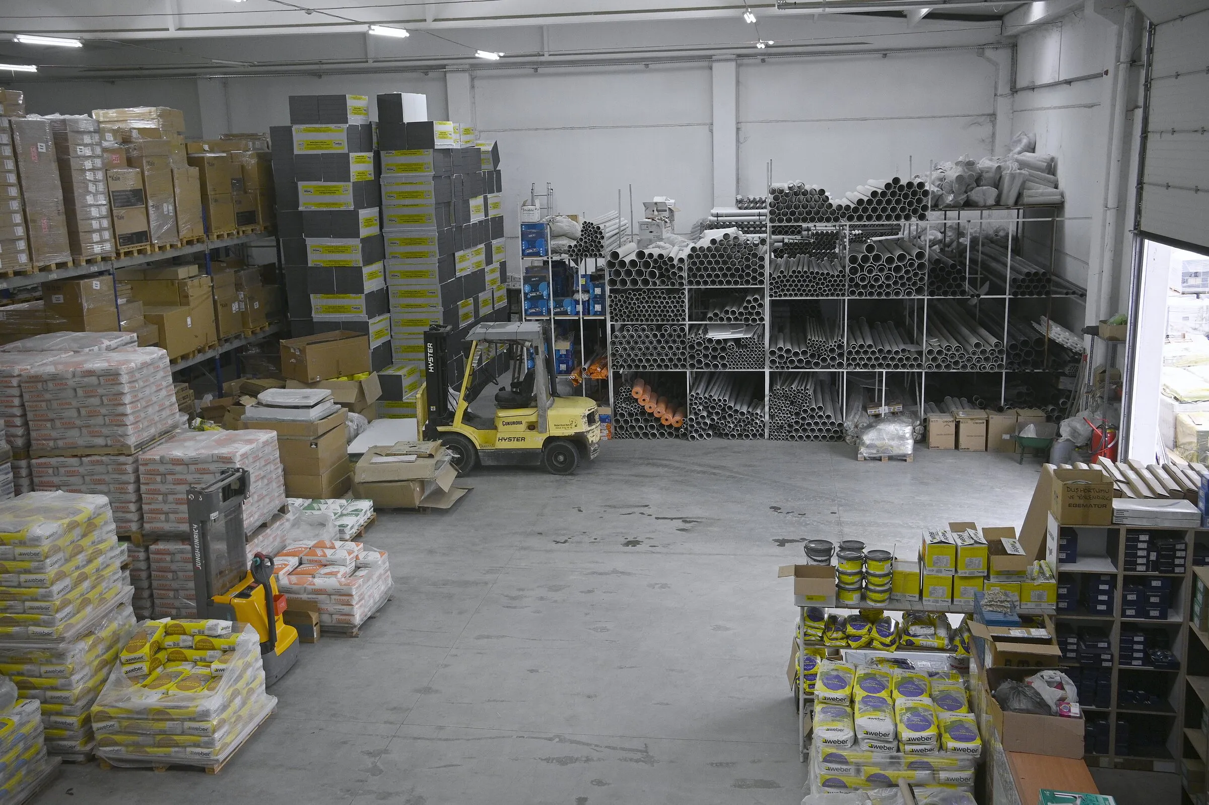 Merkezin geniş görünümü: paletlenmiş çimento torbaları, boru rafları ve forklift.