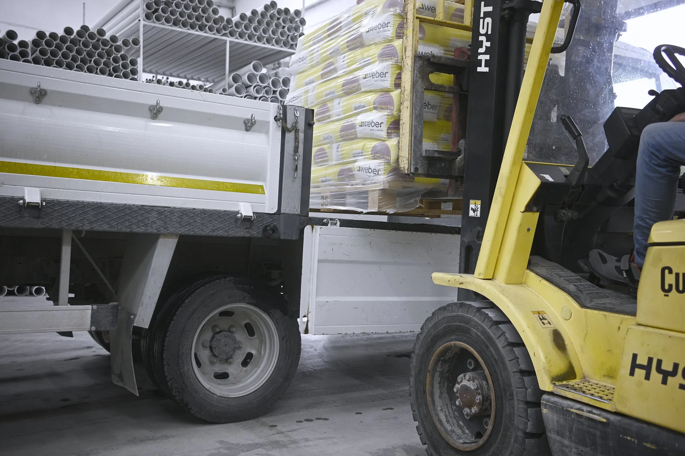 Forklift, kamyon kasasına boru ve torba malzeme yüklerken.